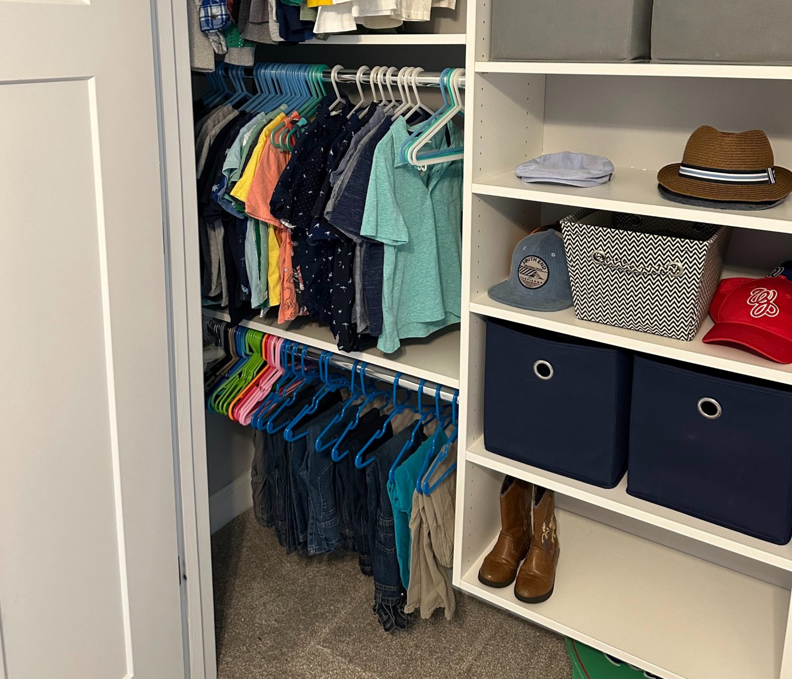 A child's closet with shirts on matching hangers and labeled fabric bins on shelves